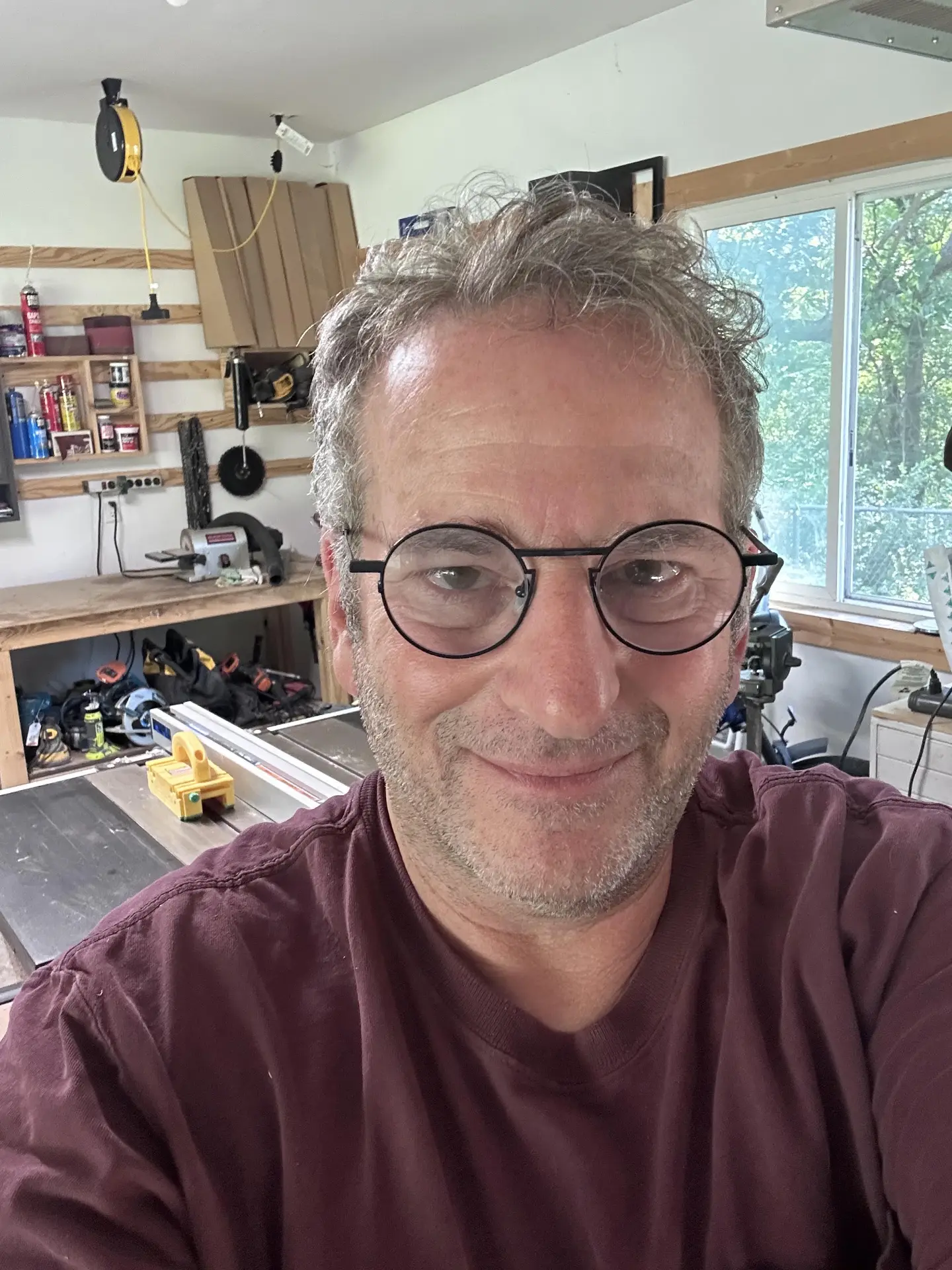 Jeff smiling in his home workshop, with a table saw and tool shelves behind him.